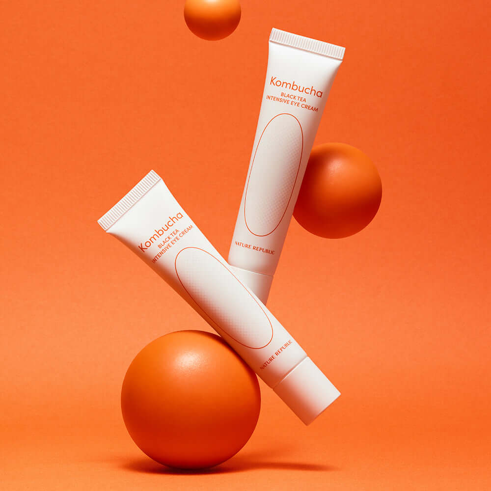 NATURE REPUBLIC Kombucha Black Tea Eye Cream 30ml tubes on an orange background with orange spheres.
