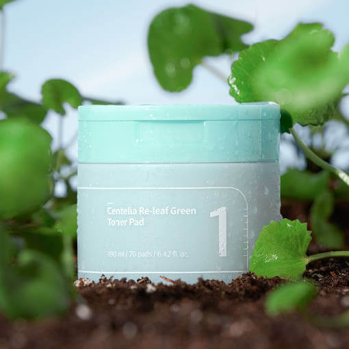 NUMBUZIN No.1 Centella Re-Leaf Green Toner Pad surrounded by lush green leaves and soil, highlighting its natural ingredients and benefits.
