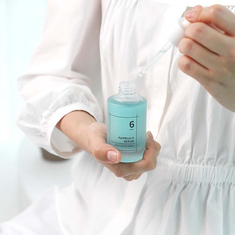 Close-up of a person holding NUMBUZIN No.6 Deep Sleep Mask Serum with dropper, white attire, enhancing night skincare routine.