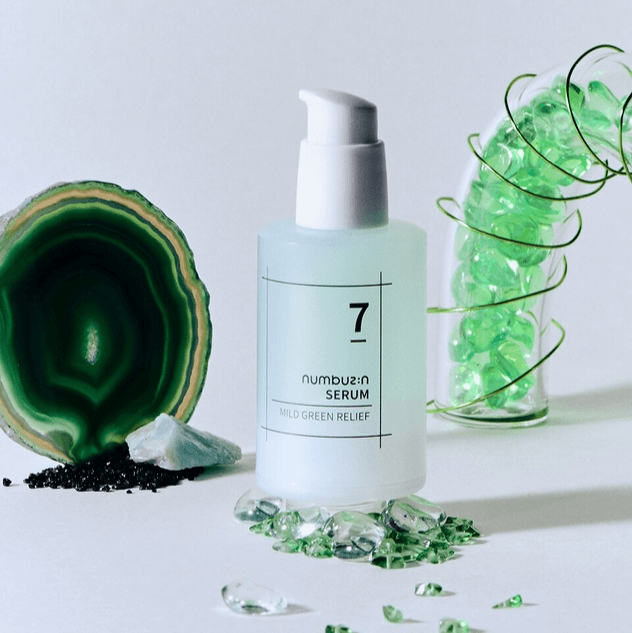 NUMBUZIN No.7 Mild Green Soothing Serum surrounded by green gemstones and agate slice, product packaging with white pump dispenser