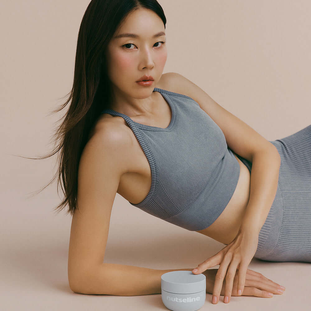 Woman posing with NUTSELINE Aroma Nut Gray Body Scrub 200g in a stylish setting.