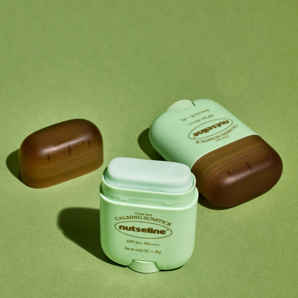 NUTSELINE Cica Nut Calming Sun Stick 18g displayed on a green background, showing product packaging and open stick.