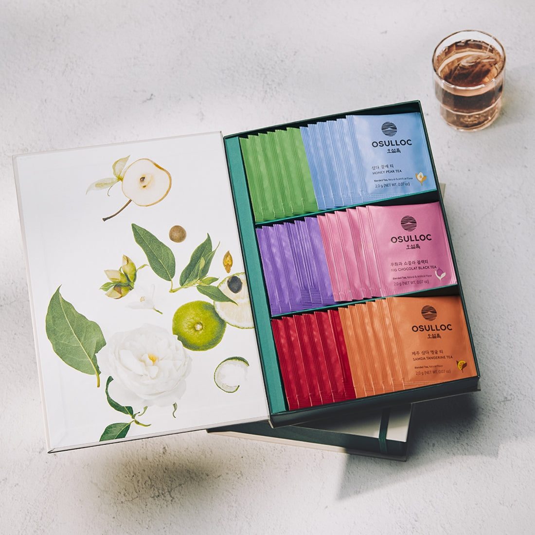 OSULLOC Tea Variation O 6 types box set with assorted tea packets displayed on a table next to a glass of tea.