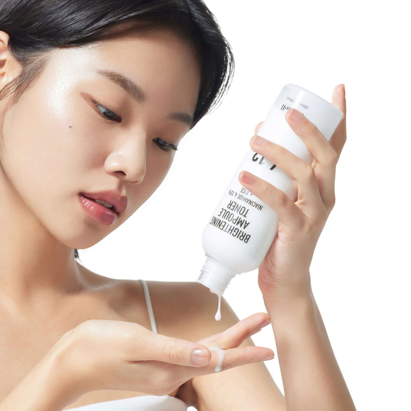 Woman applying PARNELL Niacinamide 4.12 Rice Brightening Ampoule Toner 200ml on her hand, demonstrating skincare routine.