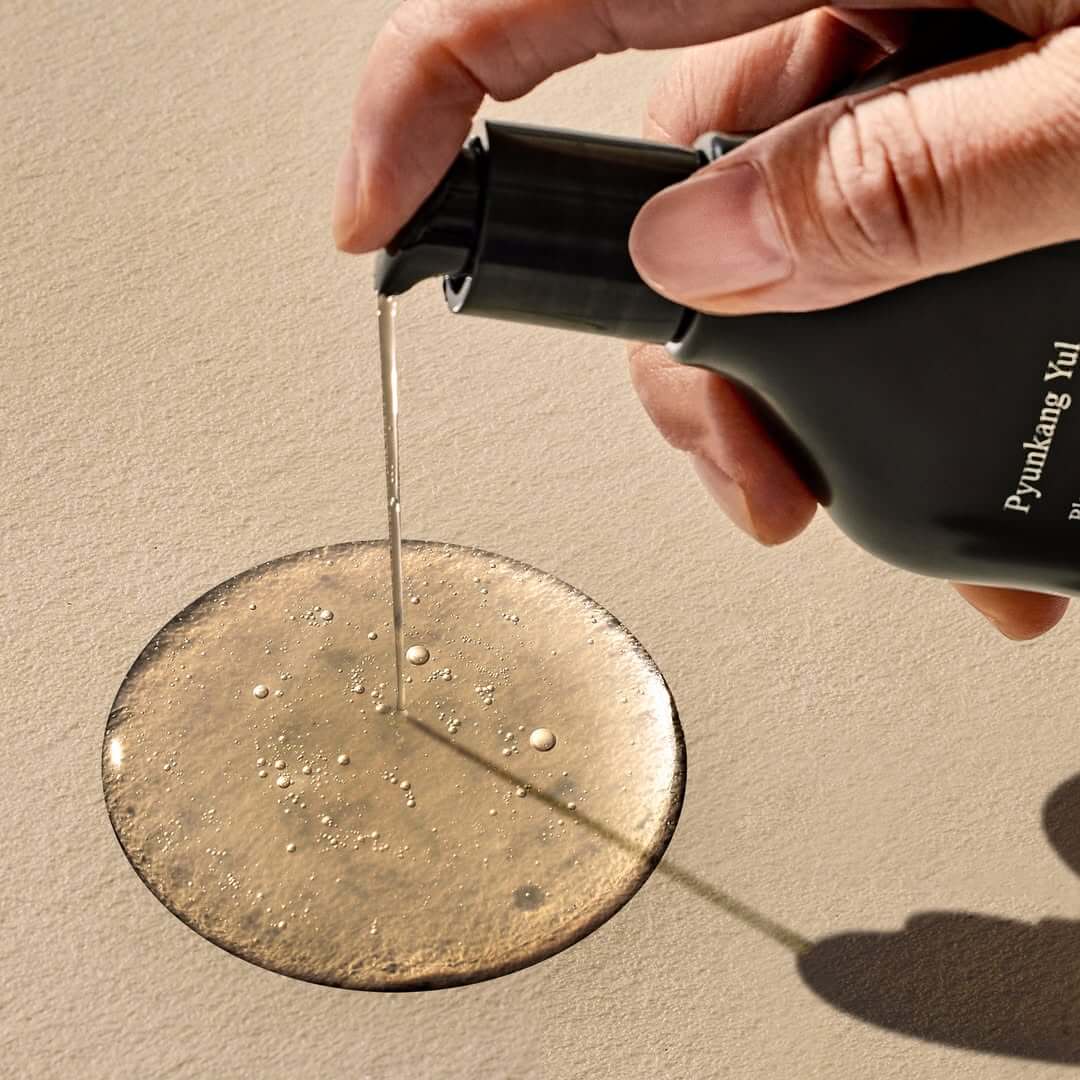 Pouring PYUNKANG YUL Black Tea Boosting Serum 45ml on surface
