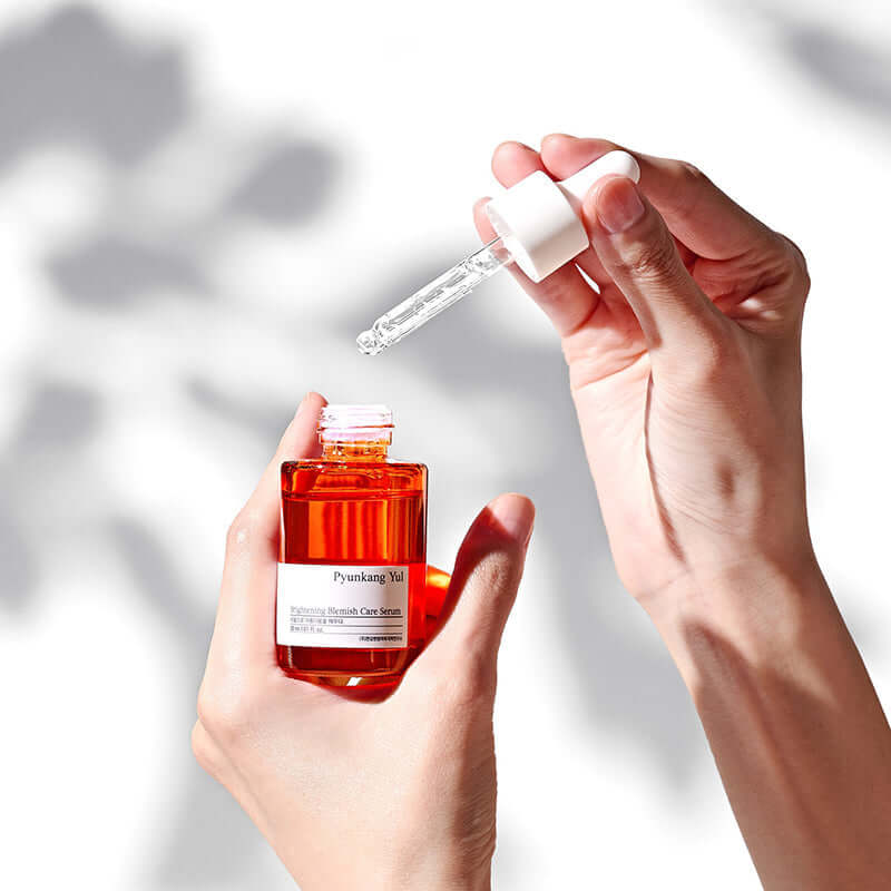 PYUNKANG YUL Brightening Blemish Care Serum 30ml in hands with dropper against light background