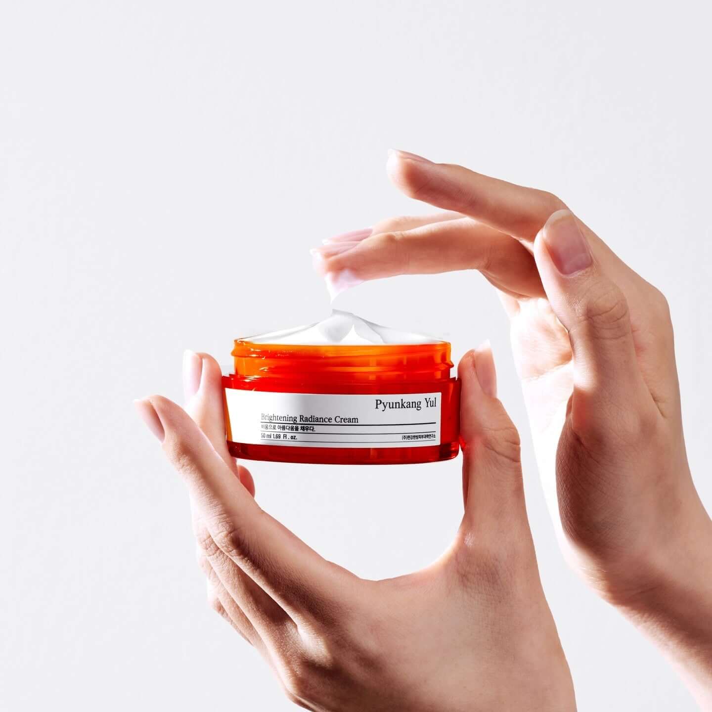 Hands holding PYUNKANG YUL Brightening Radiance Cream 50ml jar, showcasing skincare product texture and packaging.