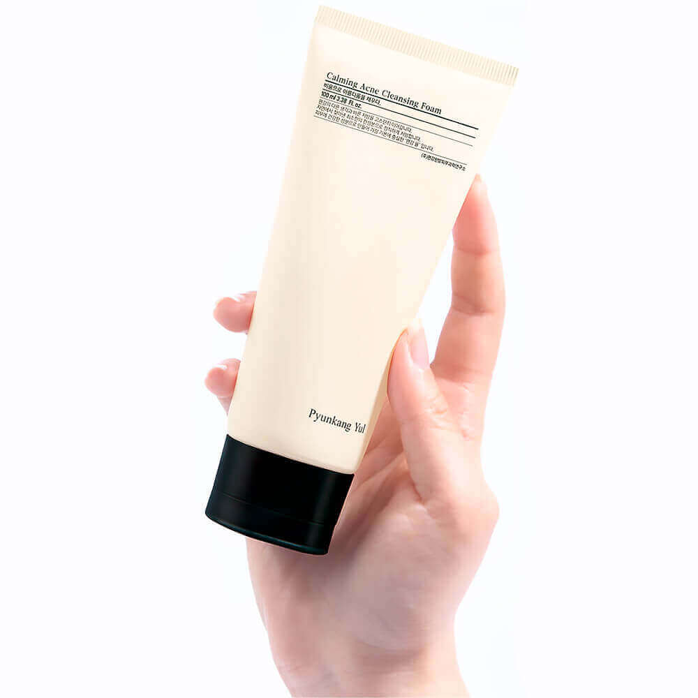 Hand holding PYUNKANG YUL Calming Acne Cleansing Foam 100ml tube on a white background.