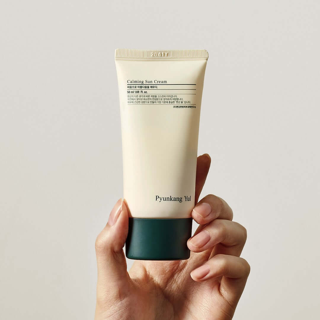 Person holding a tube of PYUNKANG YUL Calming Sun Cream SPF+PA++++ 50ml against a plain background.