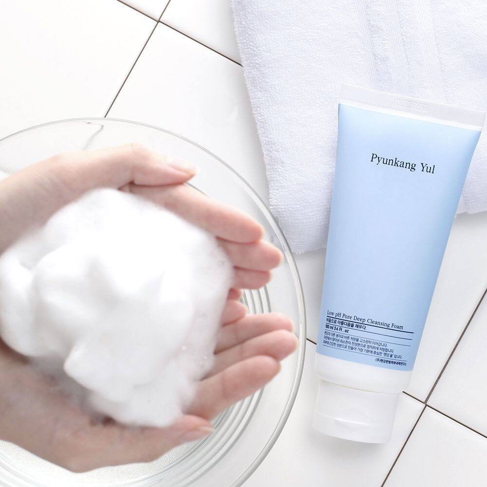 Hands with foam and PYUNKANG YUL Mildly Acidic Pore Deep Cleansing Foam 100ml on a tiled surface