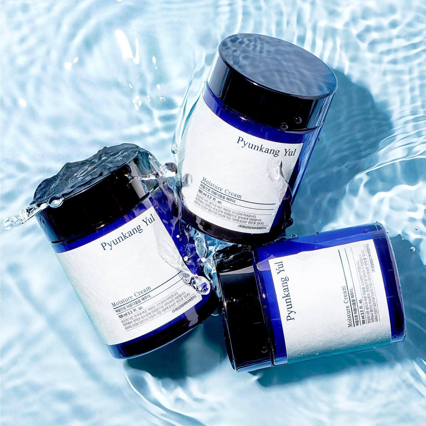 Three jars of PYUNKANG YUL Moisture Cream 100ml floating on water surface