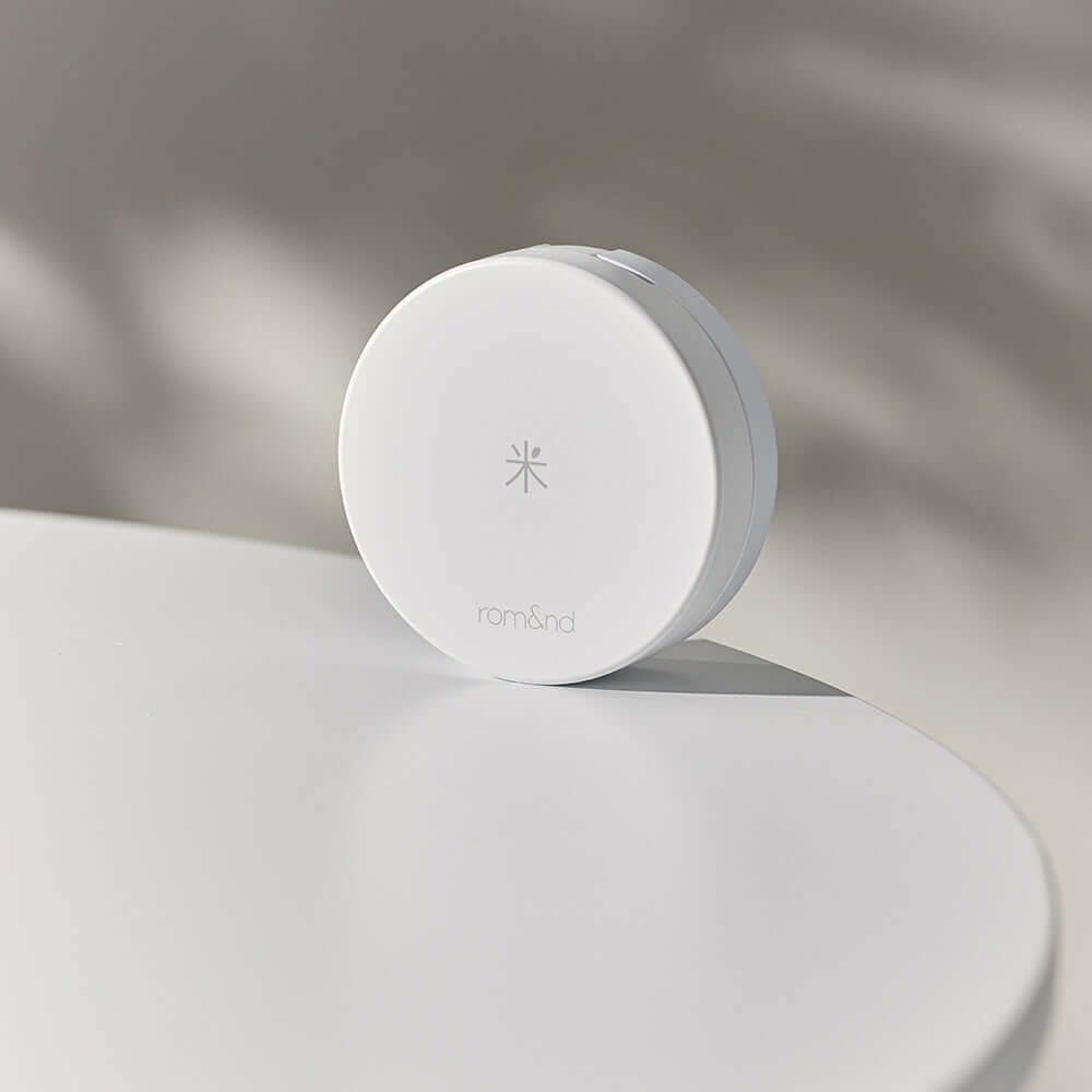 ROMAND white me tone up sun cushion on a white surface with soft shadow