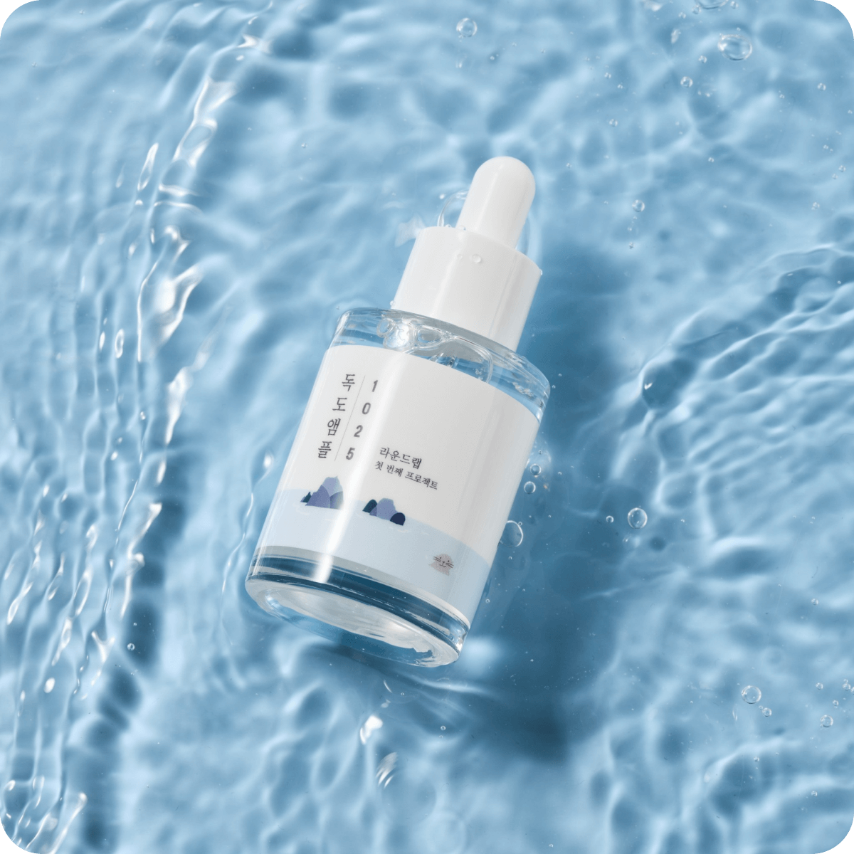 Bottle of ROUND LAB 1025 Dokdo Ampoule 45g on a water surface, showcasing skincare product design.