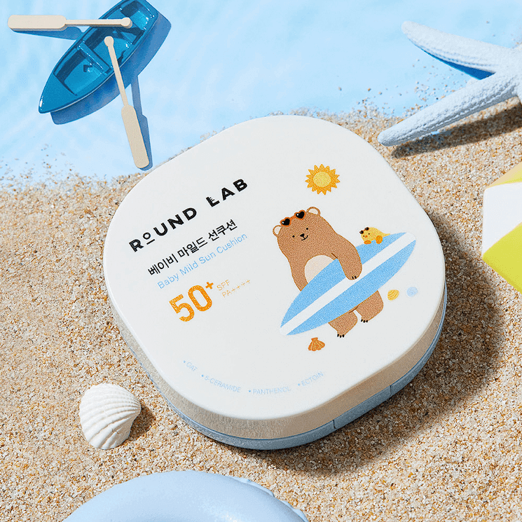 ROUND LAB Baby Mild Sun Cushion 16g on sandy beach with seashells and blue accents