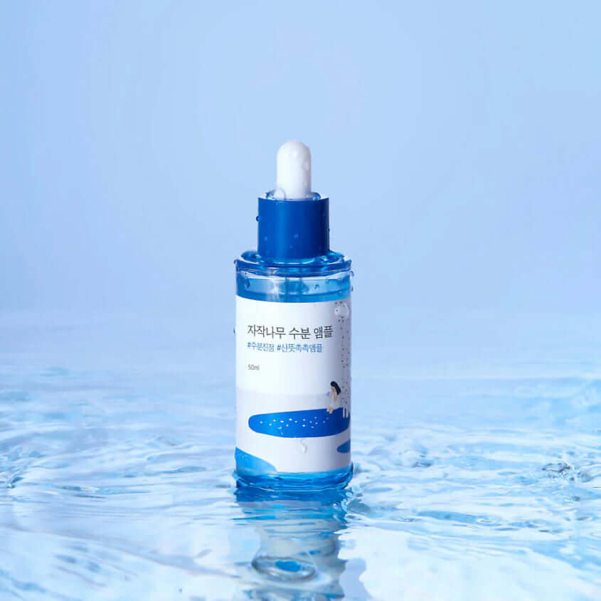ROUND LAB Birch Moisture Ampoule 50ml bottle on water surface with blue backdrop.