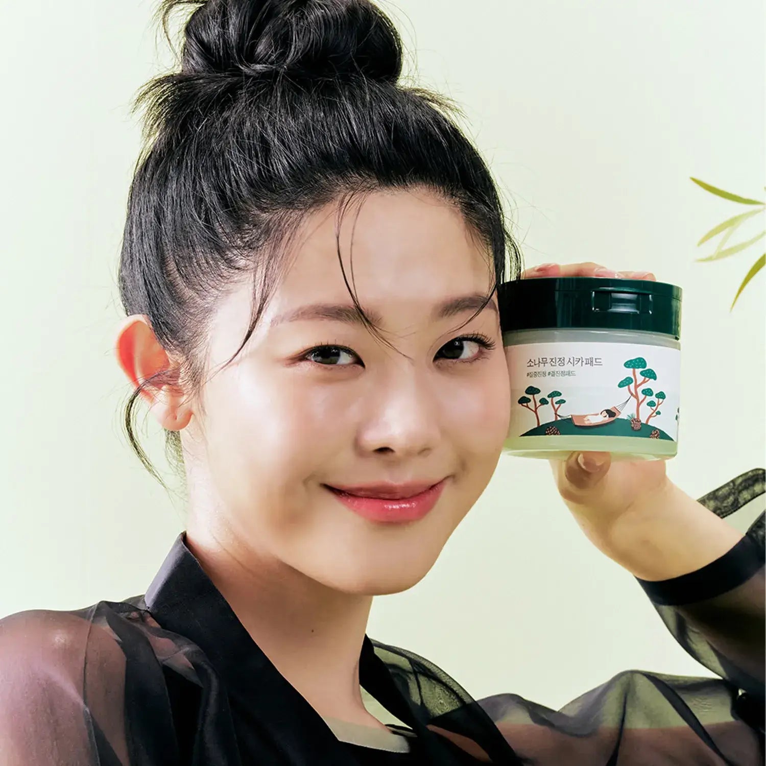 Smiling woman holding ROUND LAB Pine Calming Cica Pads 50 sheets with gentle skincare benefits.