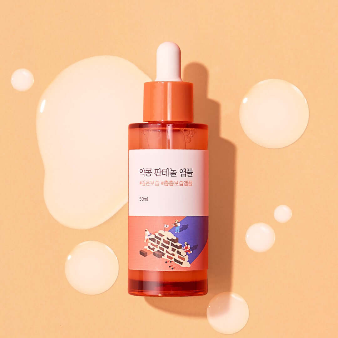 Bottle of ROUND LAB Pine Calming Cica Ampoule 30ml on peach background with liquid drops.