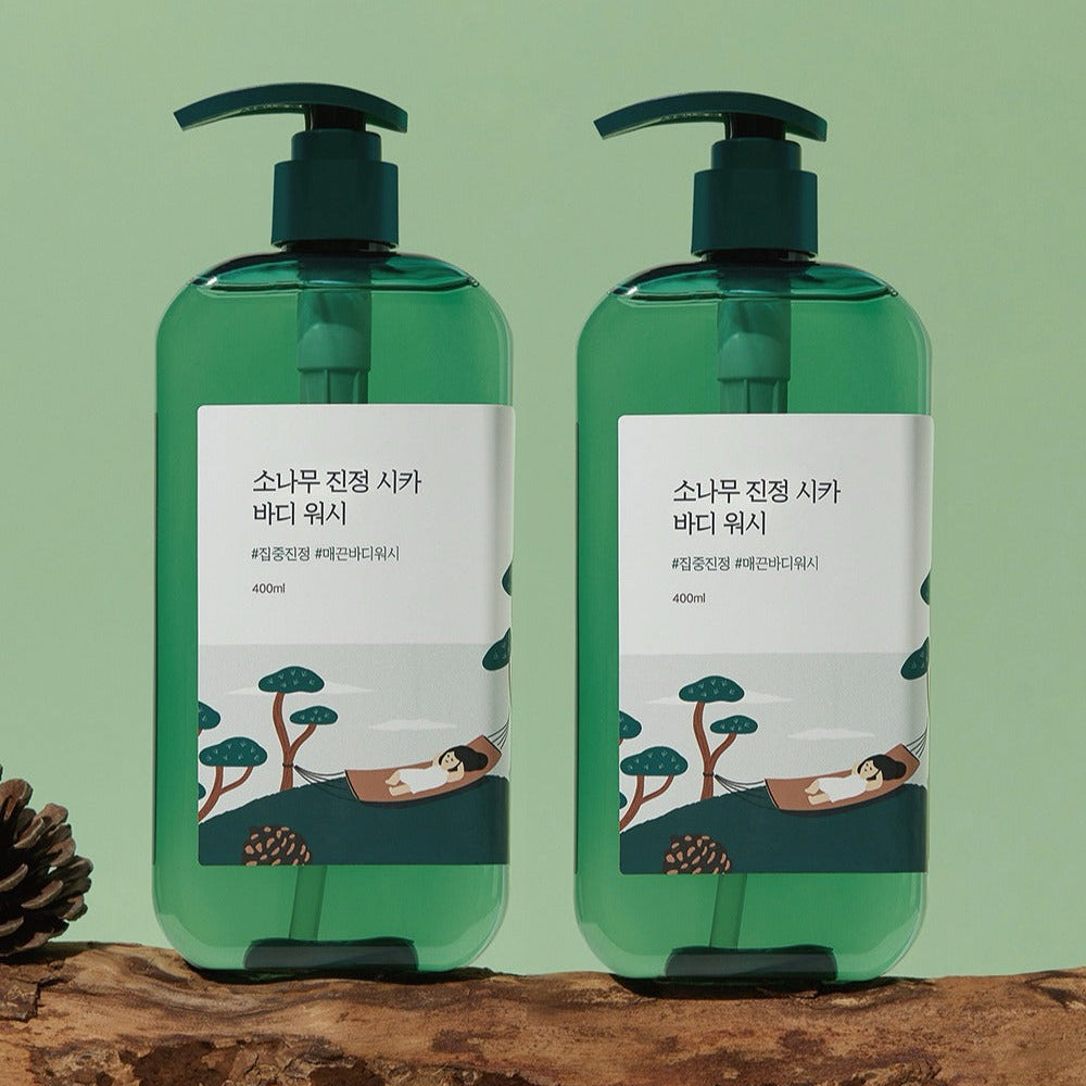 Two bottles of ROUND LAB Pine Calming Cica Body Wash 400ml with green pumps against a green background.
