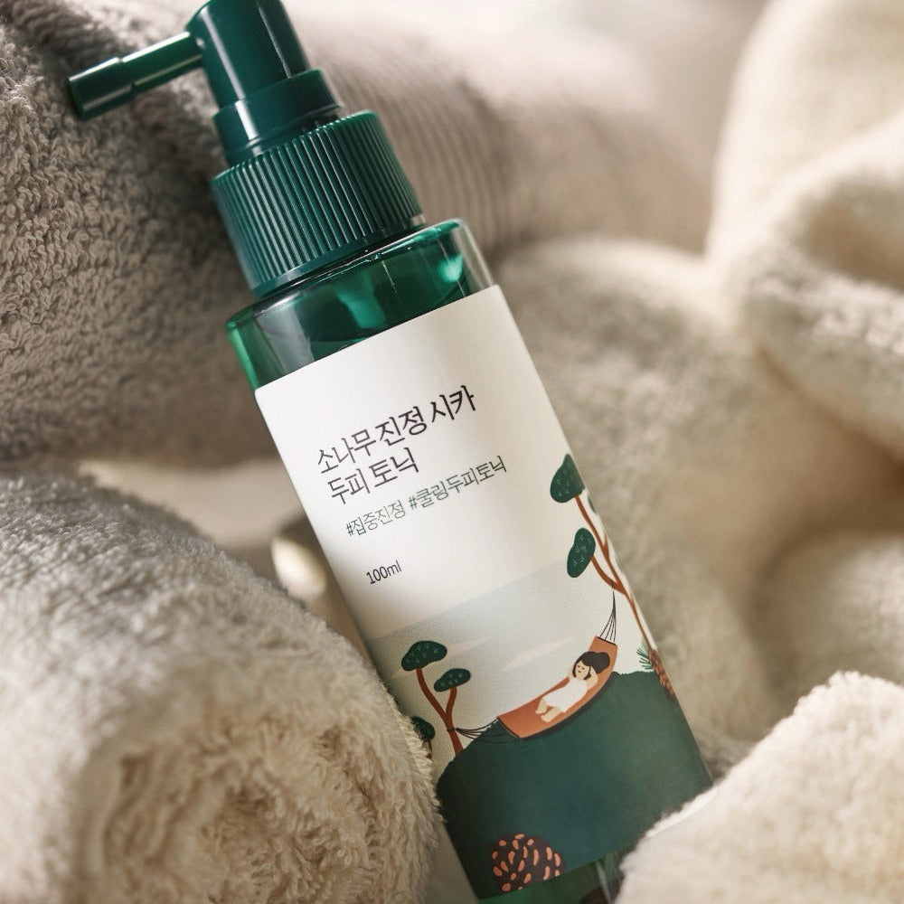 Bottle of ROUND LAB Pine Calming Cica Hair Tonic 100ml with cozy towels.
