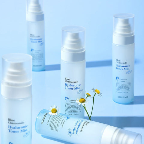 SKINFOOD Blue Chamomile Hyaluronic Toner Mist 100ml bottles arranged on a blue background with chamomile flowers.