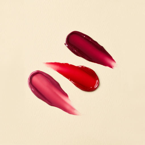 Swatches of red and pink shades of THE SAEM Saemmul Candy Syrup Gloss on a light background.