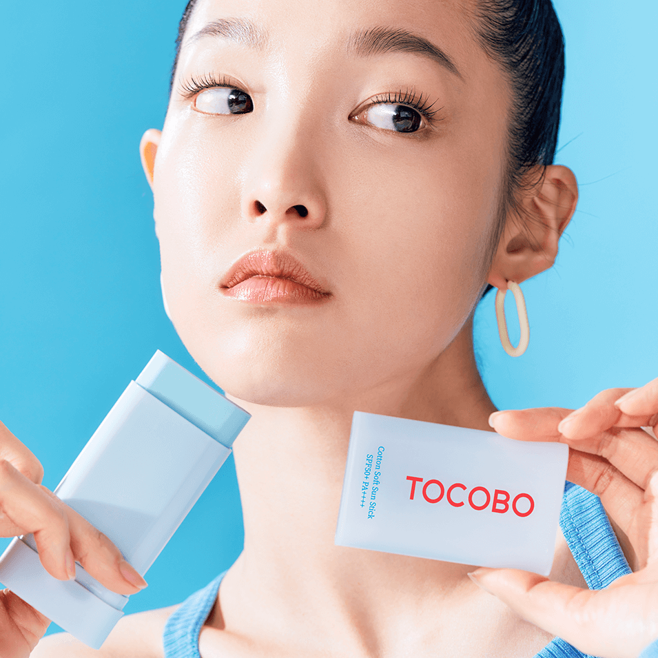 Woman holding TOCOBO Cotton Soft Sun Stick against a blue background.