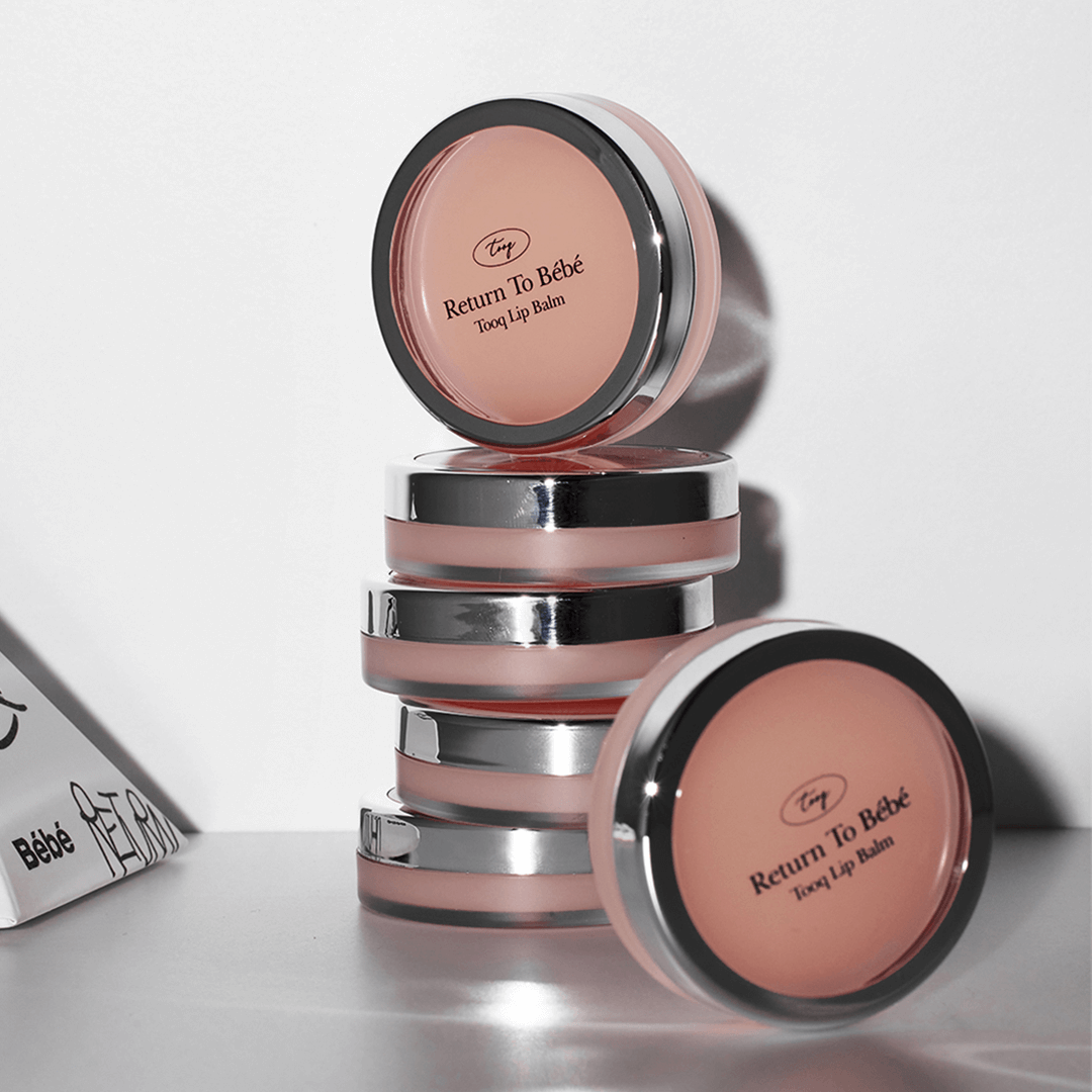 Stack of TOOQ Return To Bèbè Lip Balm containers with pink tint and sleek design.