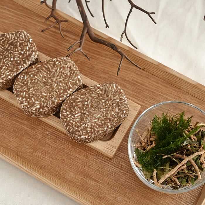 Three URANG Moringa Scalp Strengthening Shampoo Bars on a wooden tray with natural ingredients in a bowl nearby.
