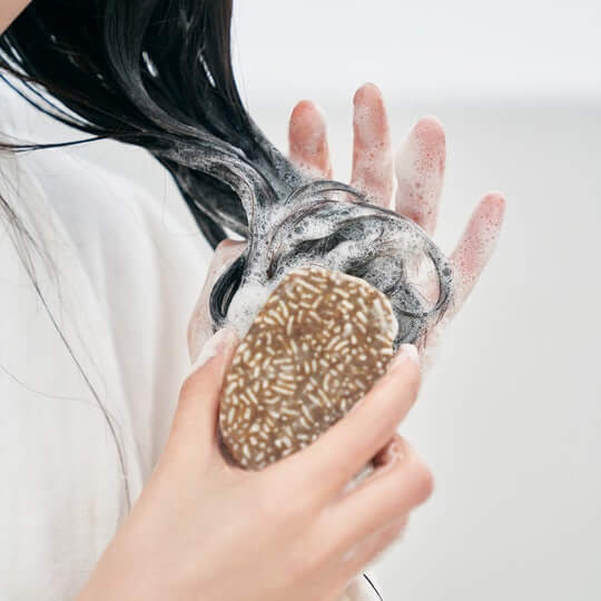 Person using URANG Moringa Scalp Strengthening Shampoo Bar to wash hair, creating lather.