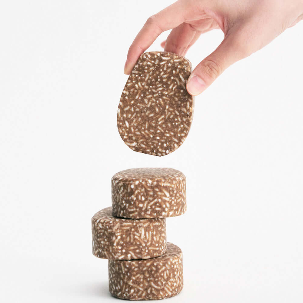 URANG Mugwort Calming Shampoo Bar being held above a stack of similar bars on white background