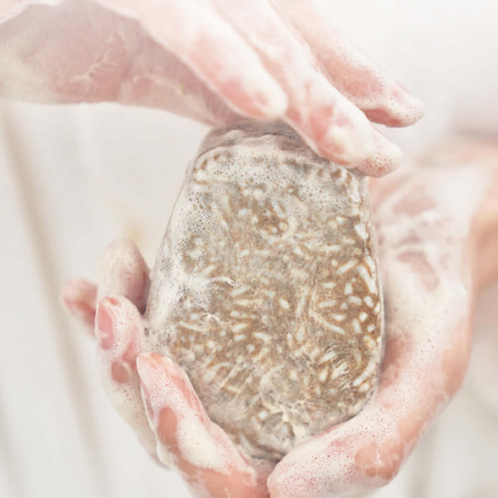 Person holding foamy URANG Mugwort Calming Shampoo Bar in hands, showcasing natural texture and soothing properties.