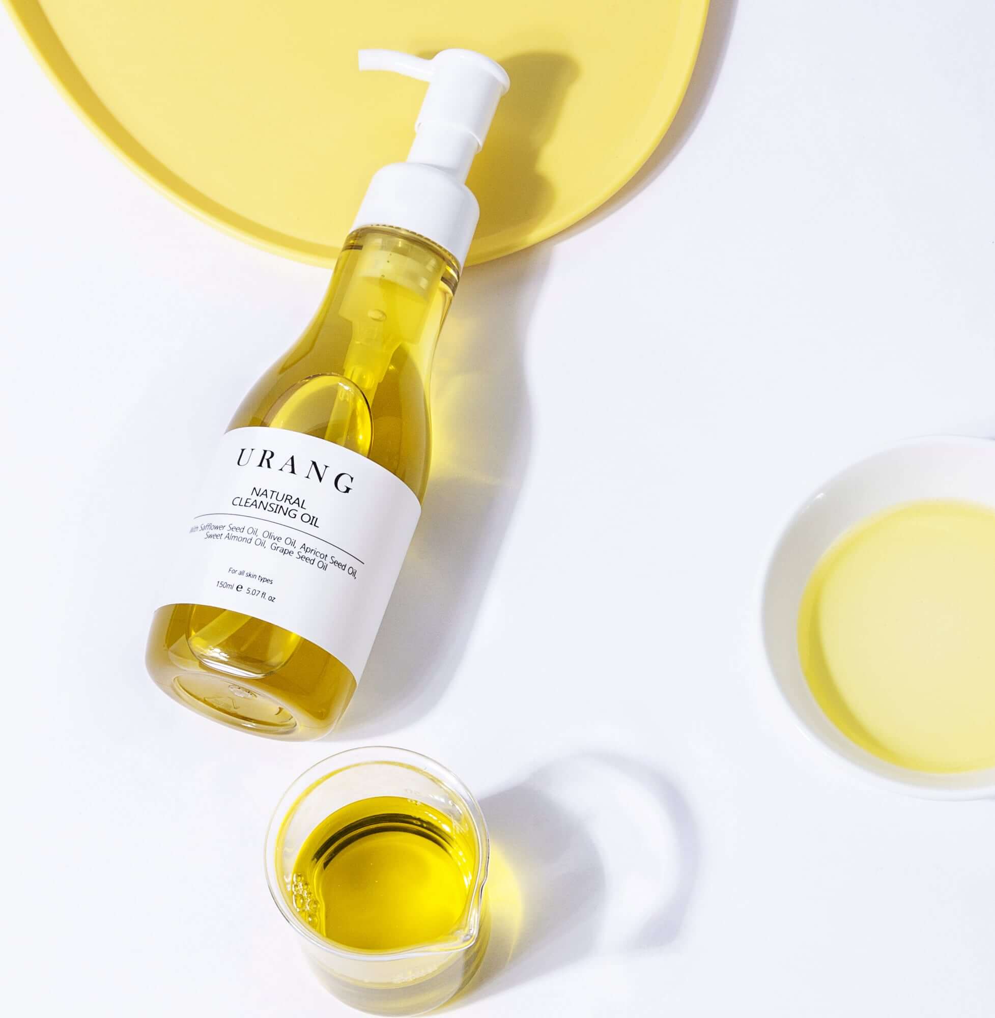 URANG Natural Cleansing Oil 150ml with yellow background and small bowls of oil, showcasing its packaging and fresh ingredients.