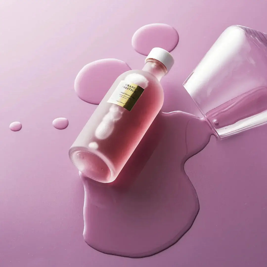 URANG Prestige Purple Shield Essence Toner bottle on spilled liquid, showcasing its luxurious rose-colored elixir on a purple surface.