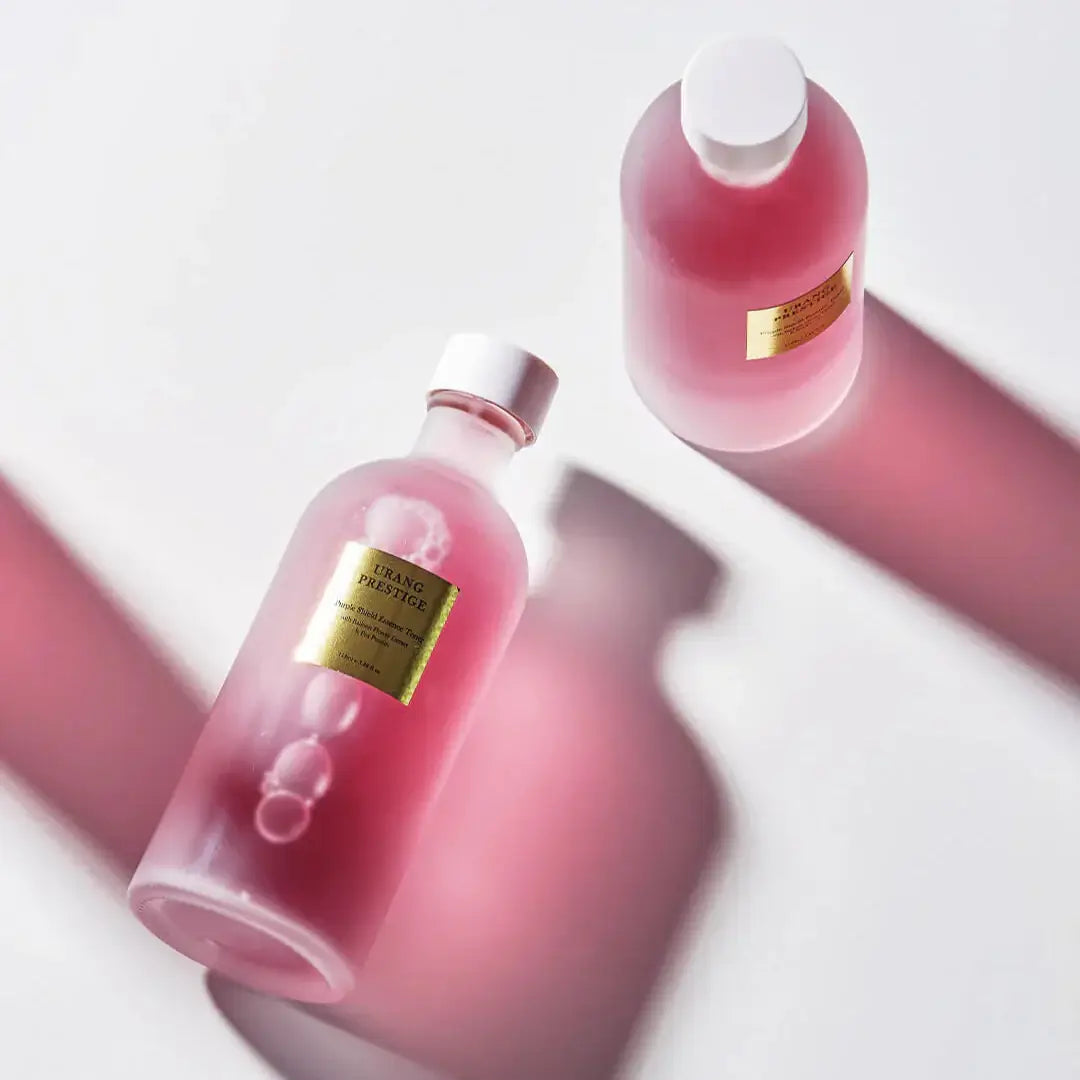 URANG Prestige Purple Shield Essence Toner bottles on a white surface with pink lighting.