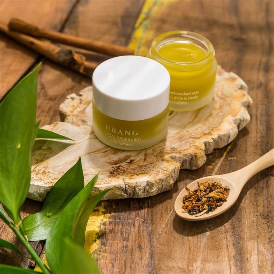 URANG SOS Multi Balm in a jar on a wooden surface with natural ingredients and foliage showcasing skincare benefits.
