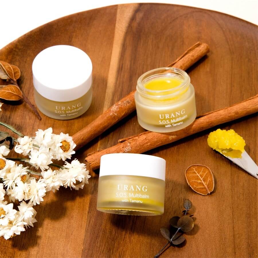 URANG SOS Multi Balm on a wooden tray with cinnamon sticks and flowers; moisturizing skincare balm with tamanu oil.