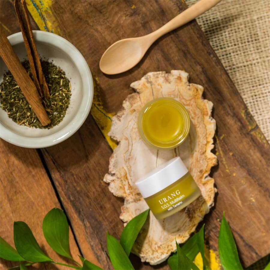 URANG SOS Multi Balm on wooden surface with herbs and spoon
