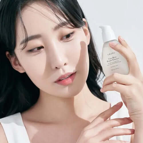 Woman holding URANG True Rose Repair Essence bottle showcasing skincare product.
