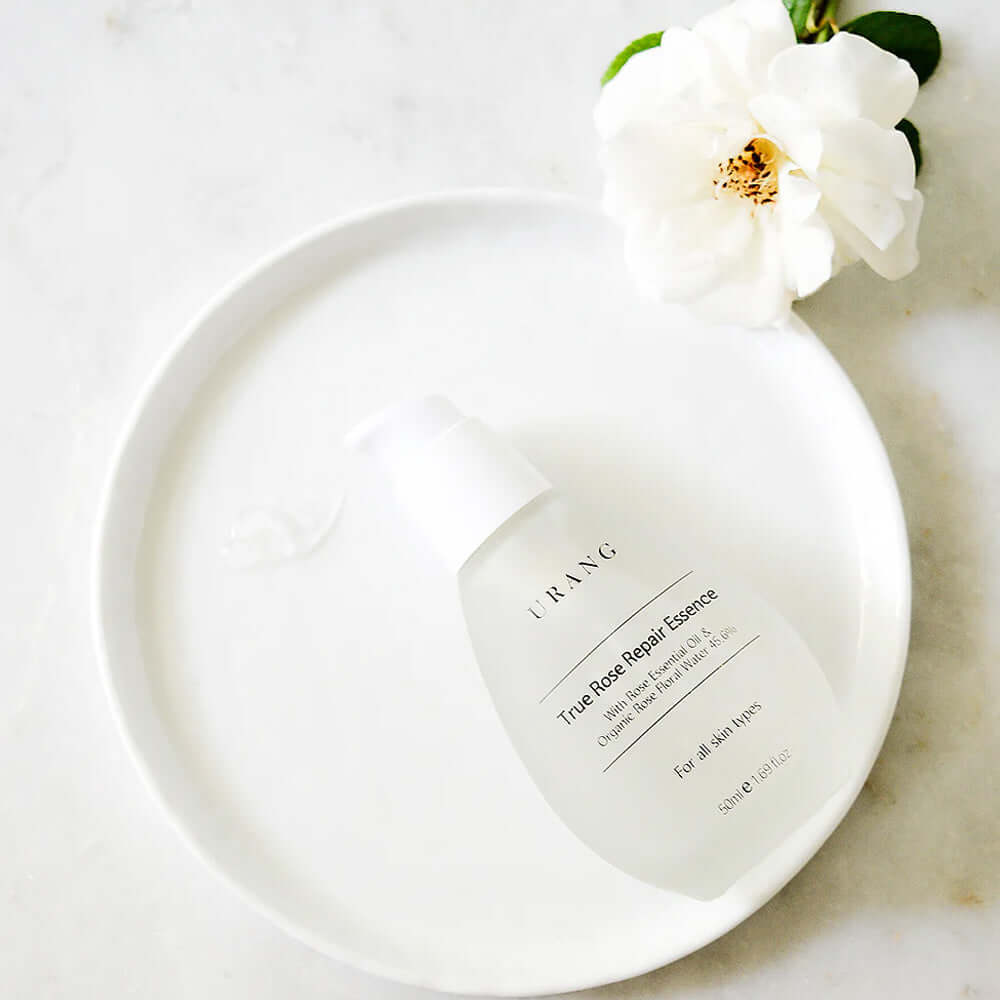 URANG True Rose Repair Essence displayed on a white plate with a white rose, highlighting premium skincare.