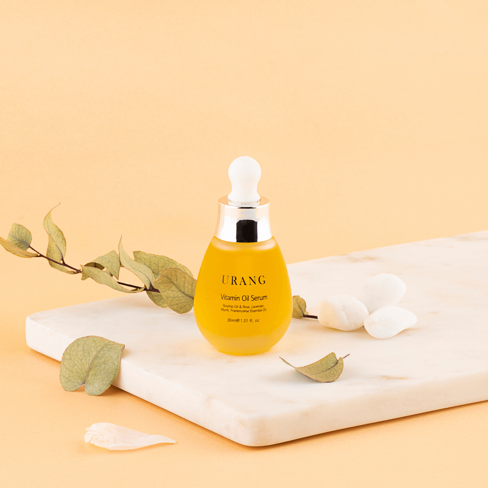 URANG Vitamin Oil Serum 30ml on marble surface with leaves and petals, highlighting luxurious skincare product