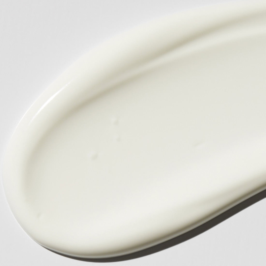 Close-up of VT COSMETIC PDRN Moist Tone-Up Sun Essence 50g's creamy texture on a smooth surface.