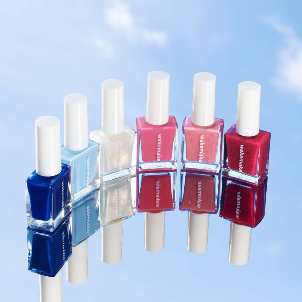 Selection of WAKEMAKE Nail Gun (#08 to #167) polishes displaying vibrant colors on a reflective surface against a sky background.