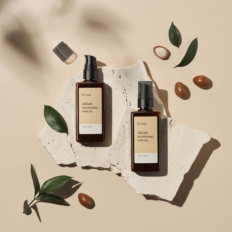 iUNIK Argan Nourishing Hair Oil 100ml bottles on textured surface with argan nuts and leaves