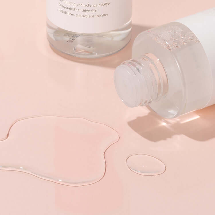 iUNIK Rose Galactomyces Essential Toner 200ml bottle with spilled liquid on a peach background.