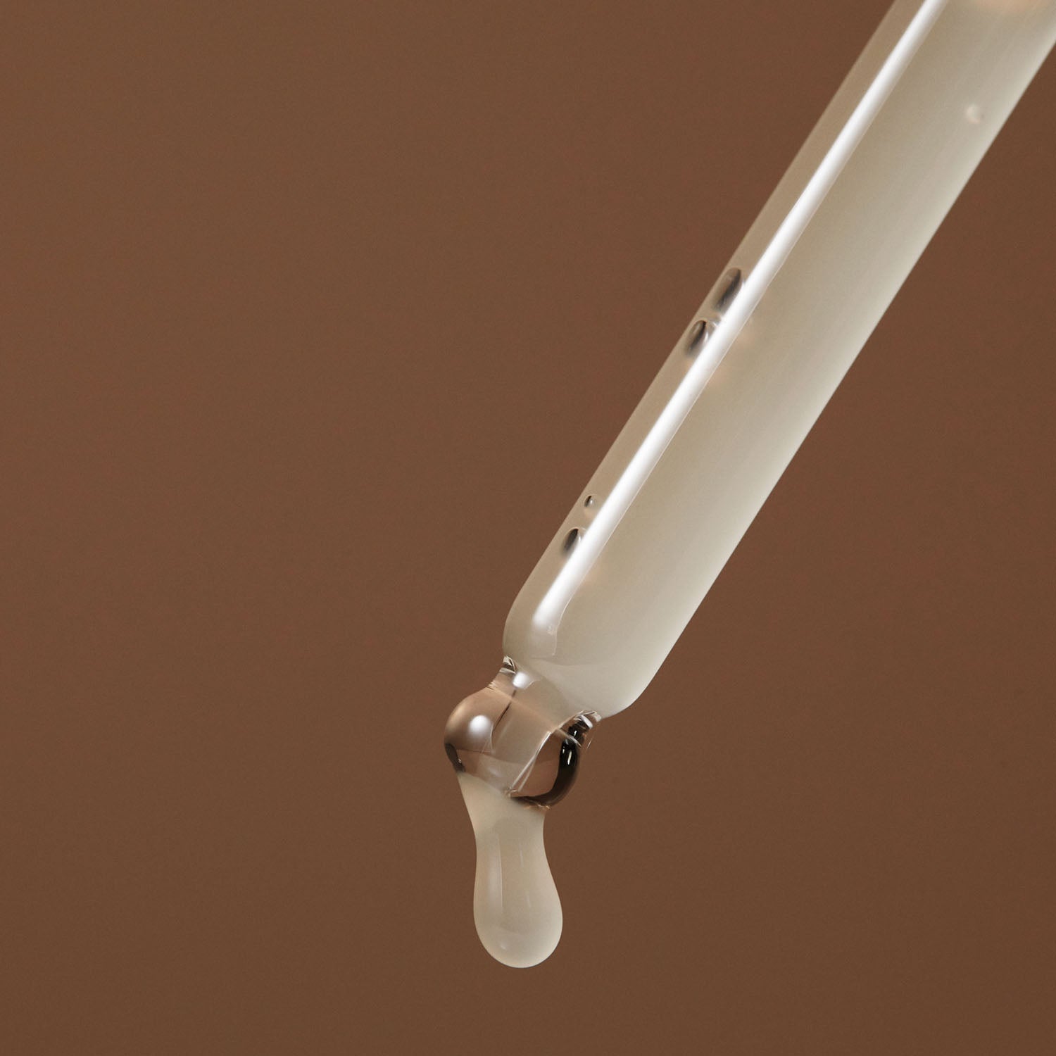 Droplet emerging from a pipette containing AROMATICA Vitalizing Rosemary Elasticity Ampoule 30ML on a brown background.