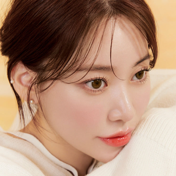 Close-up of a person with brown hair and warm skin tone, wearing a white sweater and pearl earrings, gazing thoughtfully.
