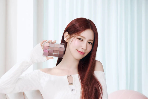 Woman showcasing eyeshadow palette from Wake Make: Unveiling the Artistry of Korean Beauty Innovation, in a bright room.