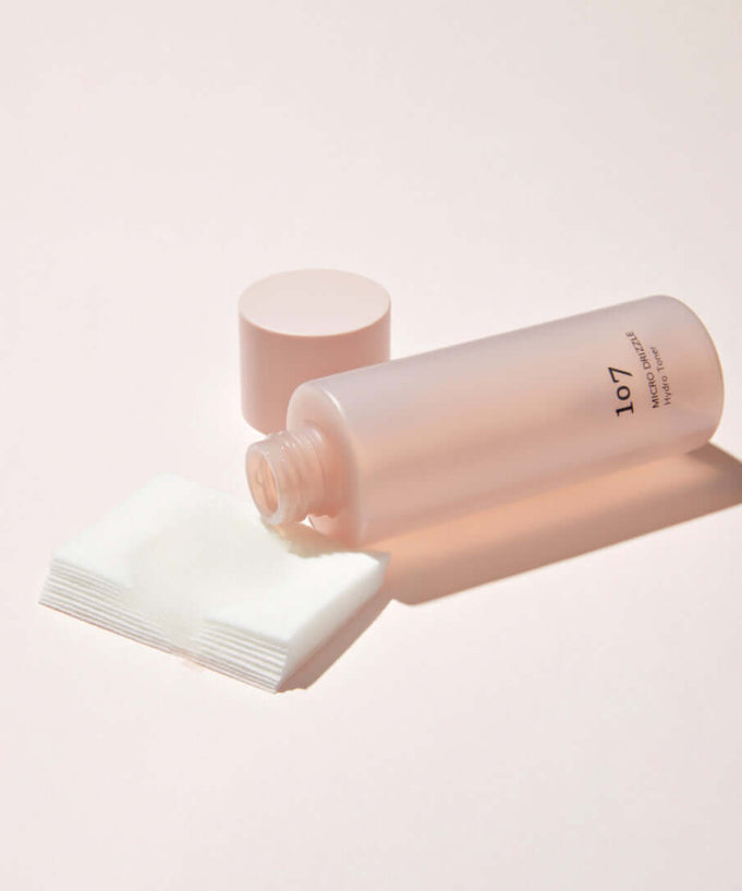 107 Micro Drizzle Hydro Toner 155ml bottle with open cap and cotton pads on a light background.