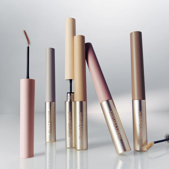 Assorted HEART PERCENT Dot On Mood Fake Up Brow Cara tubes in various shades on a reflective surface.