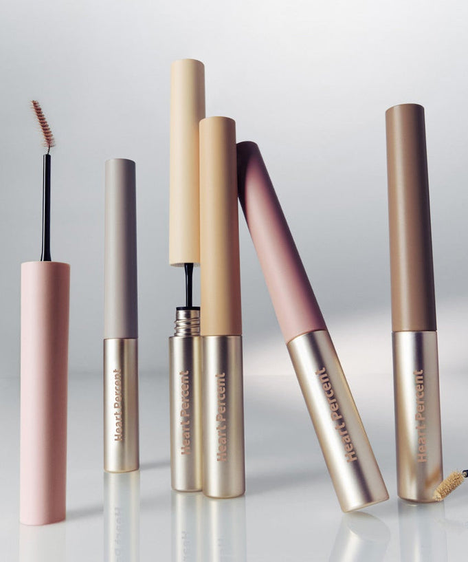 Assorted HEART PERCENT Dot On Mood Fake Up Brow Cara tubes in various shades on a reflective surface.